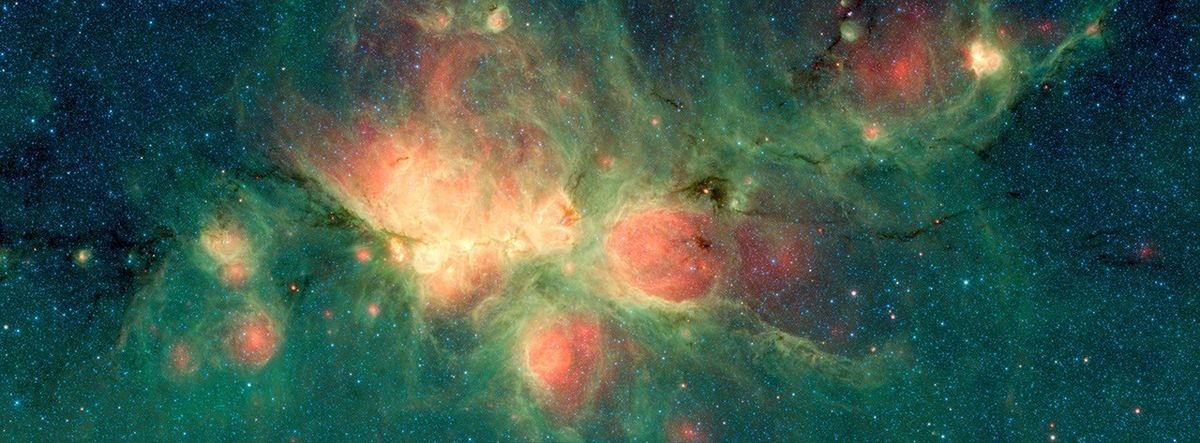 Red bubbles and green clouds of gas and dust in a Spitzer infrared image of the Cat’s Paw Nebula.