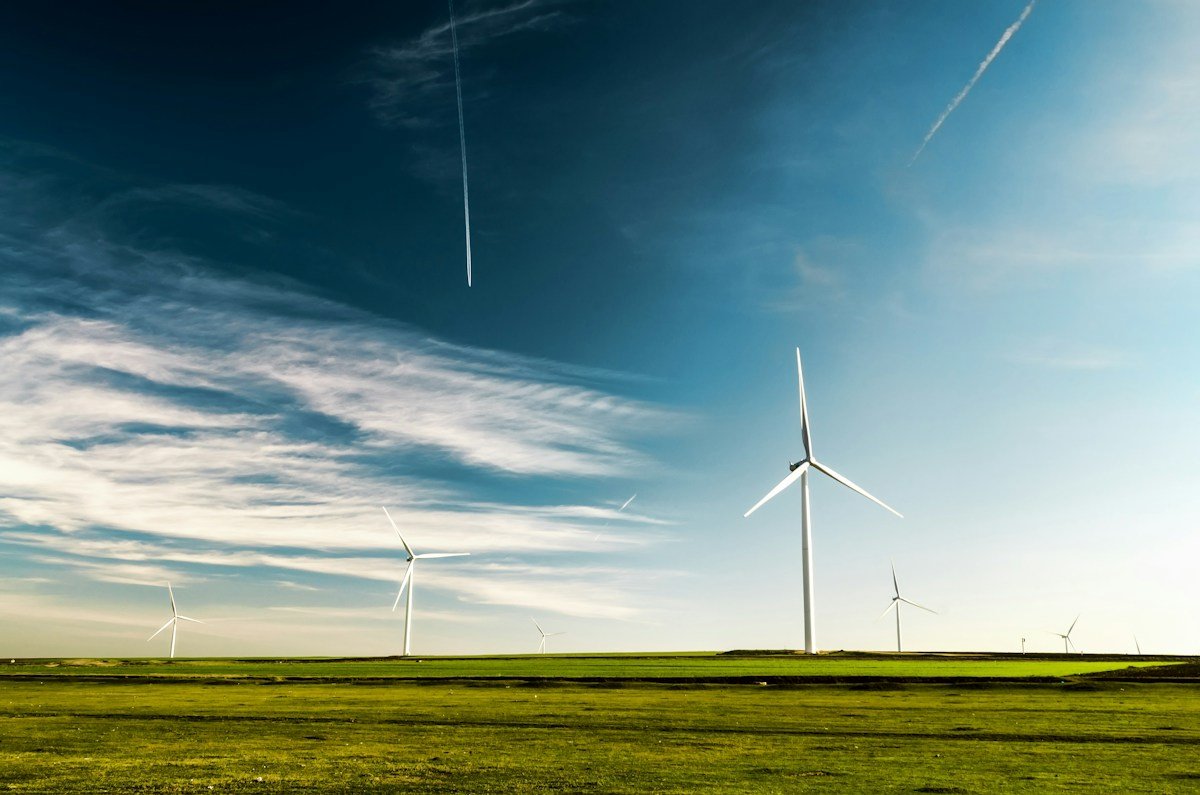 White wind turbines stand across a green field under a blue sky with thin clouds.
